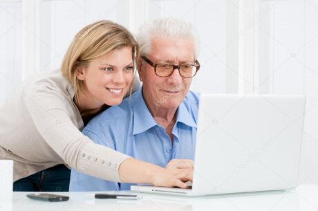 Älteres Paar sitzt entspannt vor einem Laptop und bekommt Hilfe.